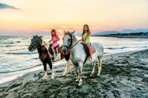 Twin sisters riding horses in the sunset by the sea on the island of Ada Bojana, Montenegro