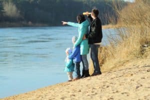 Family standing on the side of the river with their kids pointing at something