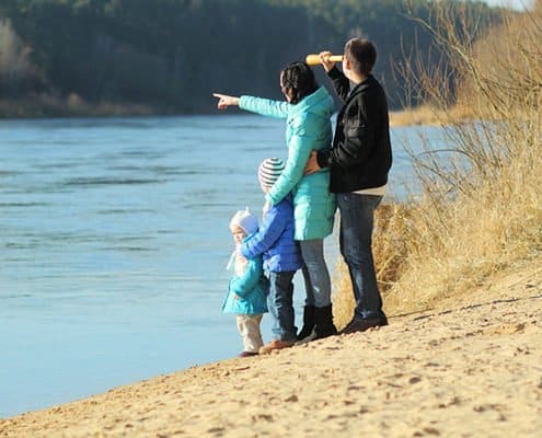 Family standing on the side of the river with their kids pointing at something