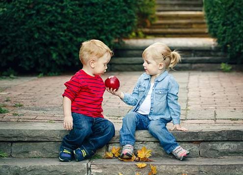 2 kids on a side walk sharing a red apple.