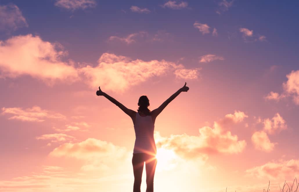 Girl standing and raising her hands over sunset