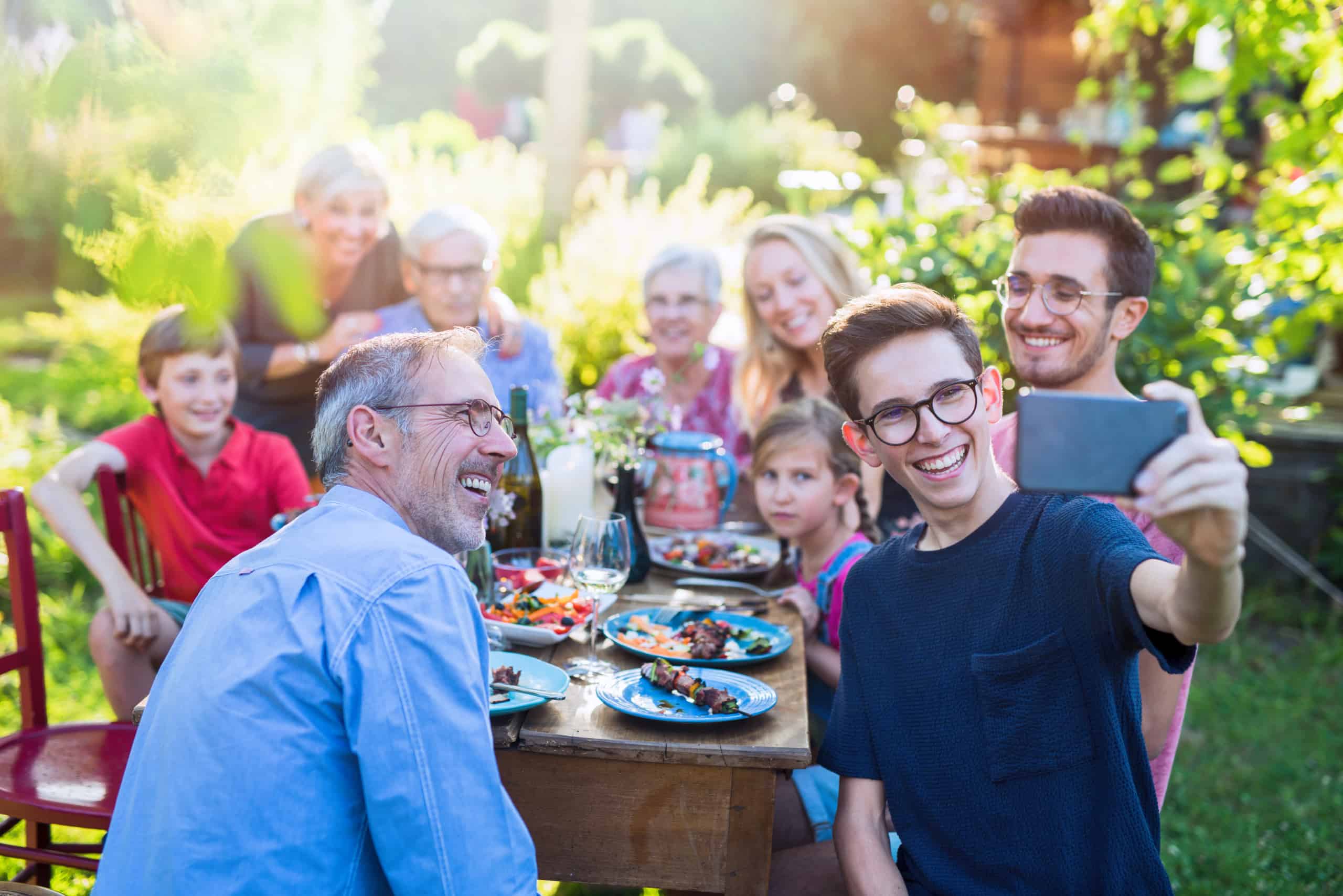  A happy family is gathered around a table in a backyard, decorated with lights and balloons, and they are taking a selfie together.